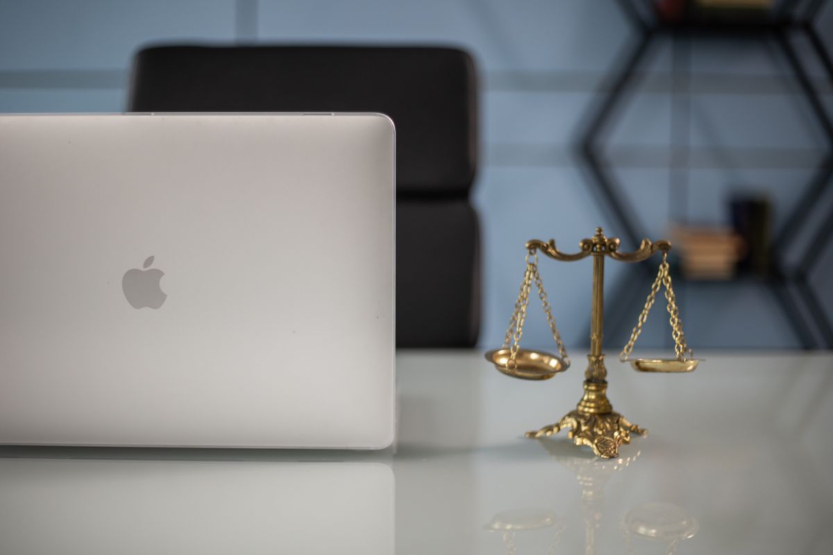 A laptop open on a desk next to a small scales of justice